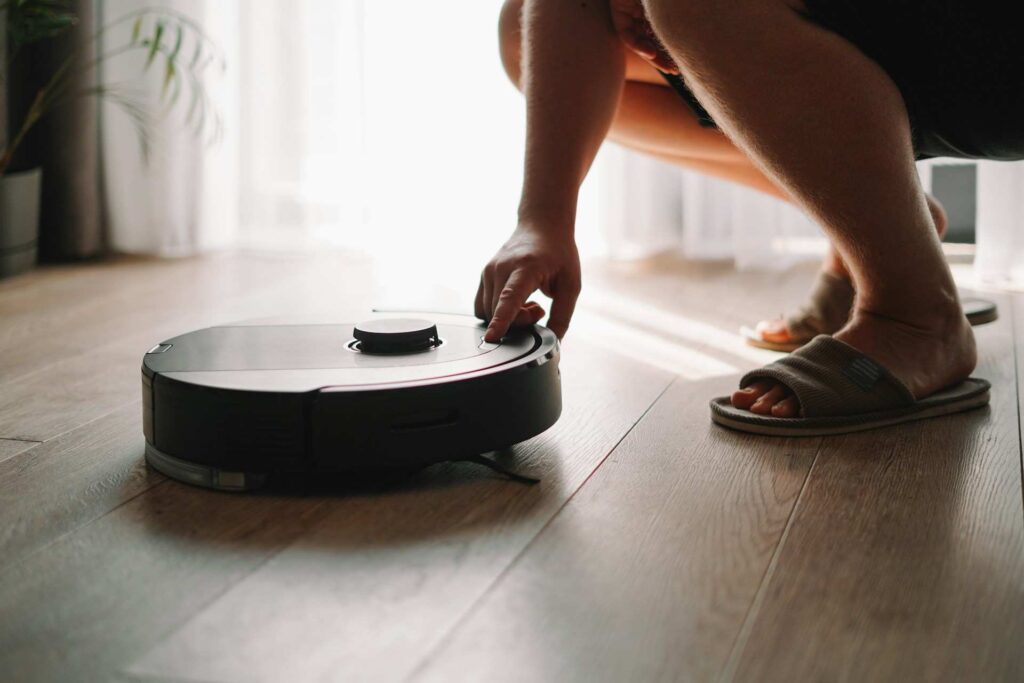 Kéz indítja el a robotporszívót a fapadlón